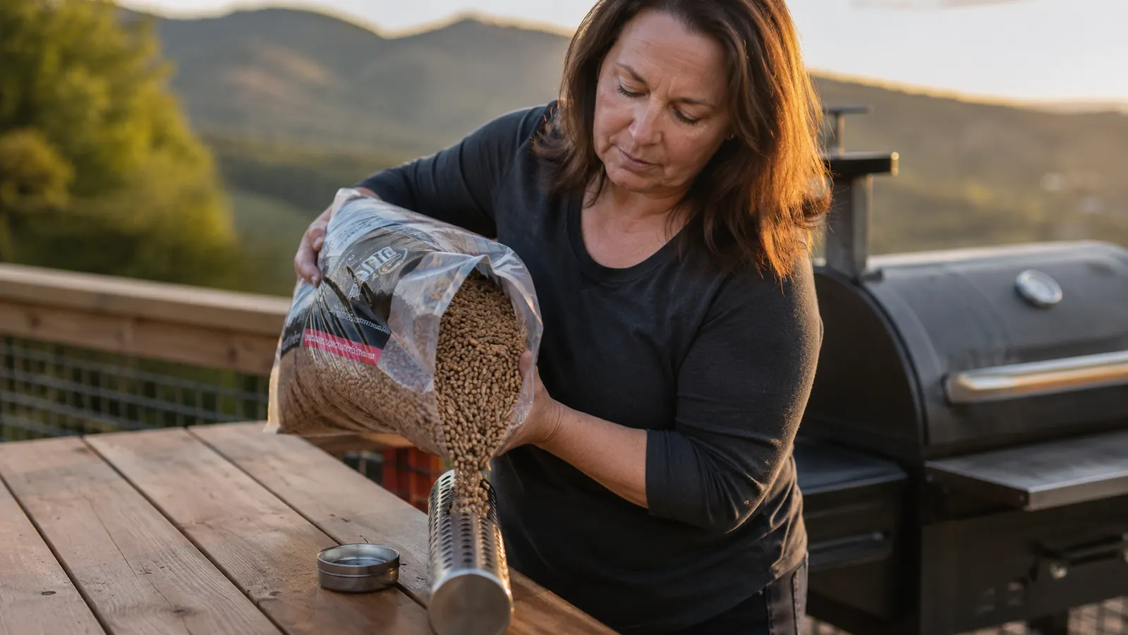 Gwen sprinkling wood pellets into a smoker tube on the back deck in the East Bay hills at golden hour