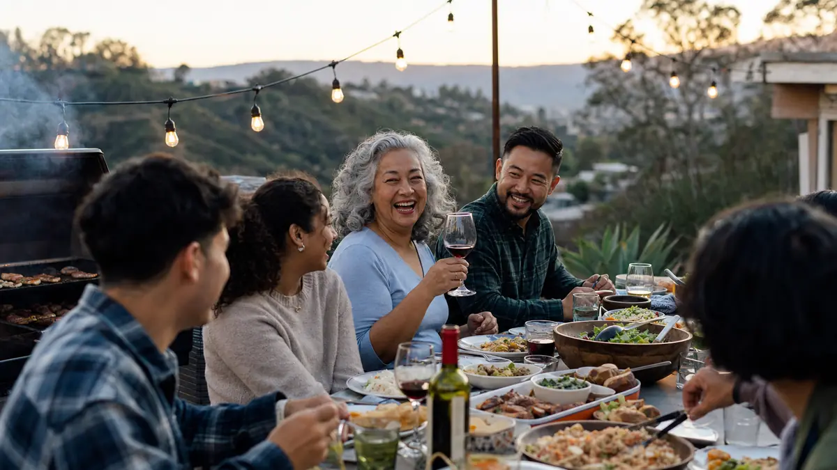 Extended family gathered around a long backyard table for a Sunday cookout with a grill smoking in the background